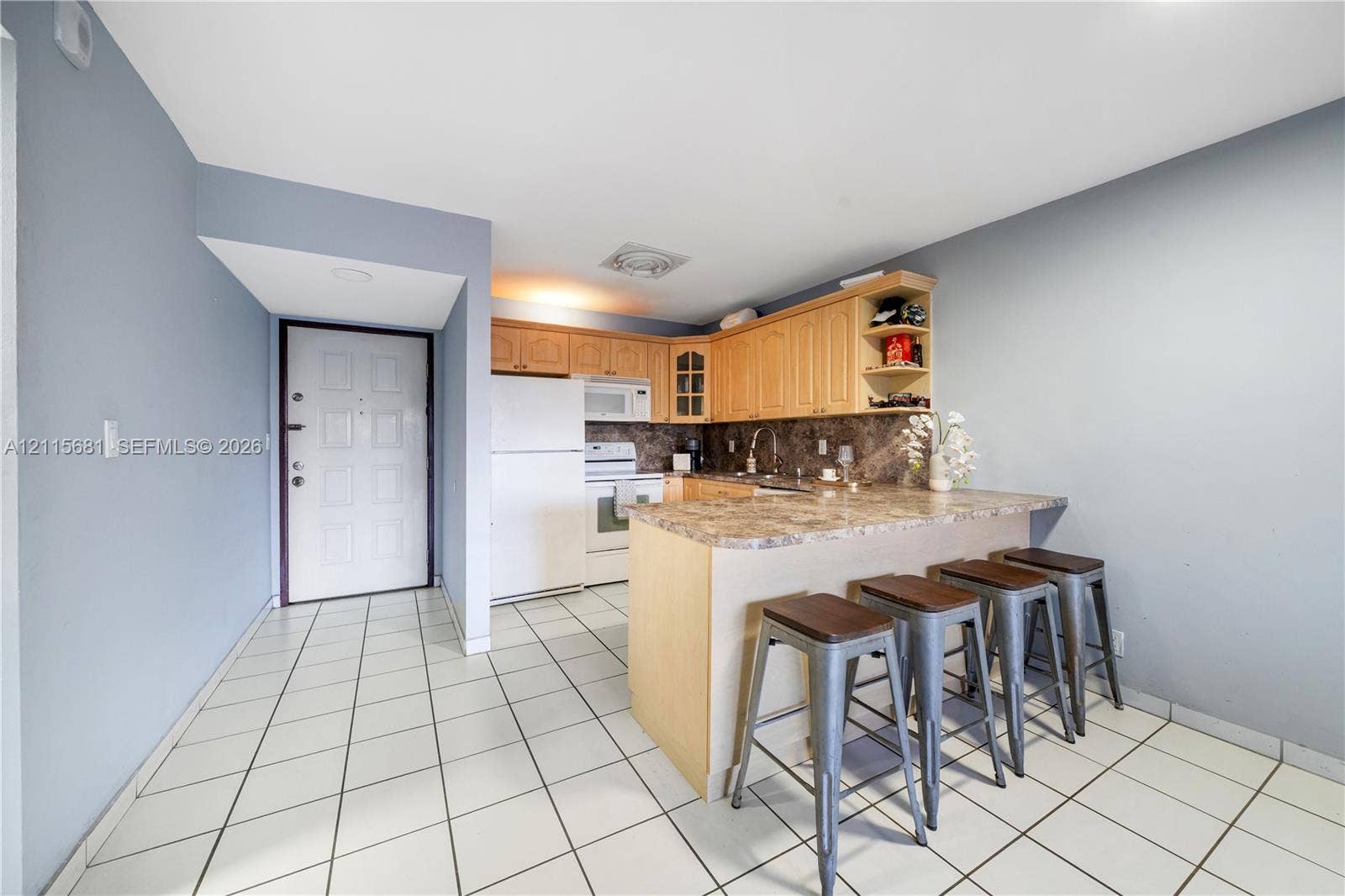 Kitchen featuring light-finish cabinetry, stone-patterned countertops, a breakfast bar, and tile flooring