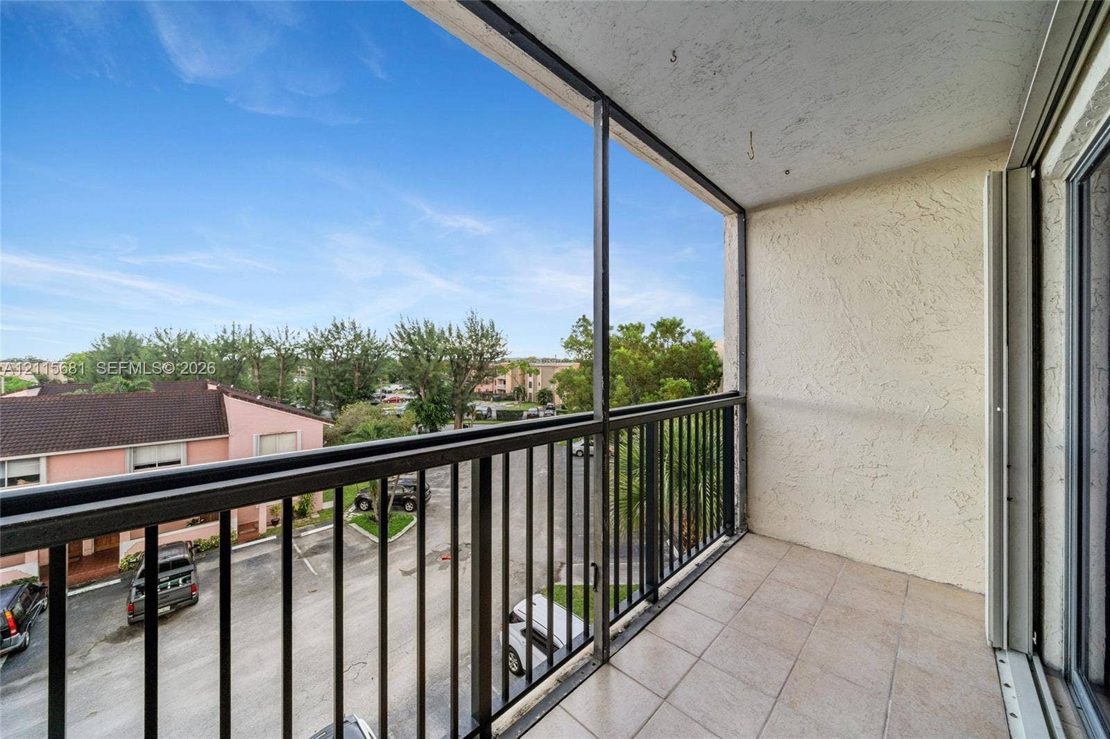 Covered balcony featuring tile flooring, textured wall surfaces, and a metal railing enclosure
