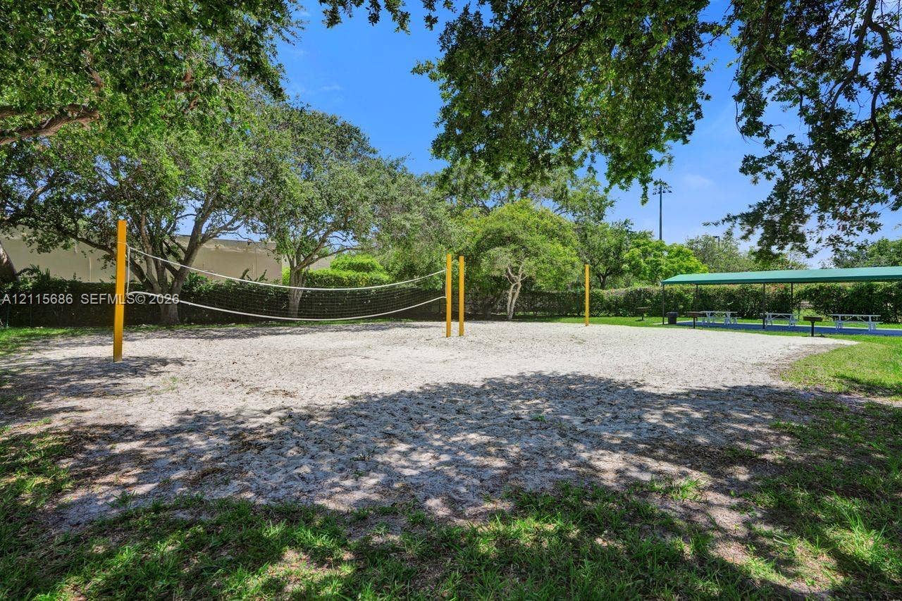 8946 SW 150th Ct Circle E, Miami, Miami, FL 33196 Sand volleyball court featuring a netted boundary, perimeter landscaping, mature shade trees, and a covered pavilion