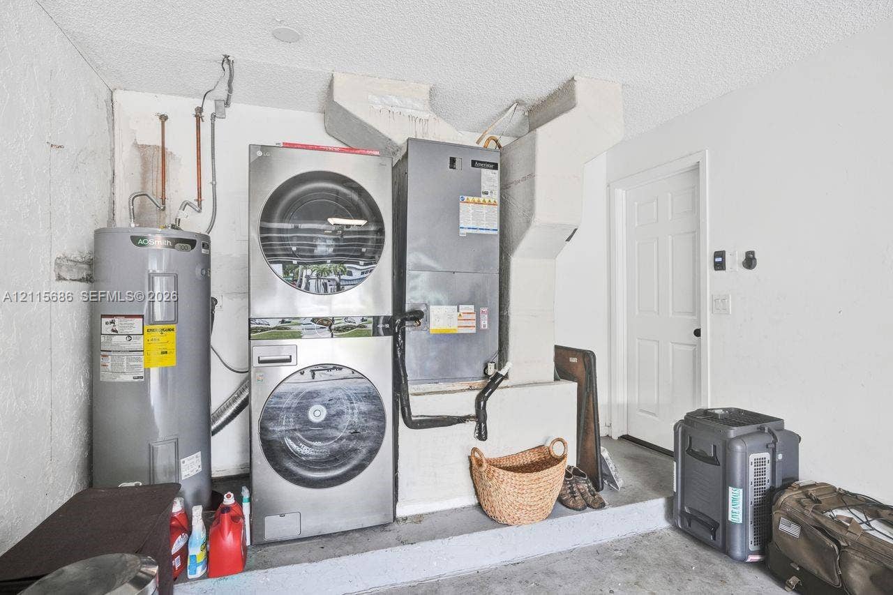 8946 SW 150th Ct Circle E, Miami, Miami, FL 33196 Utility area featuring a stacked stainless steel laundry unit, a vertical water heater, and an integrated climate control system