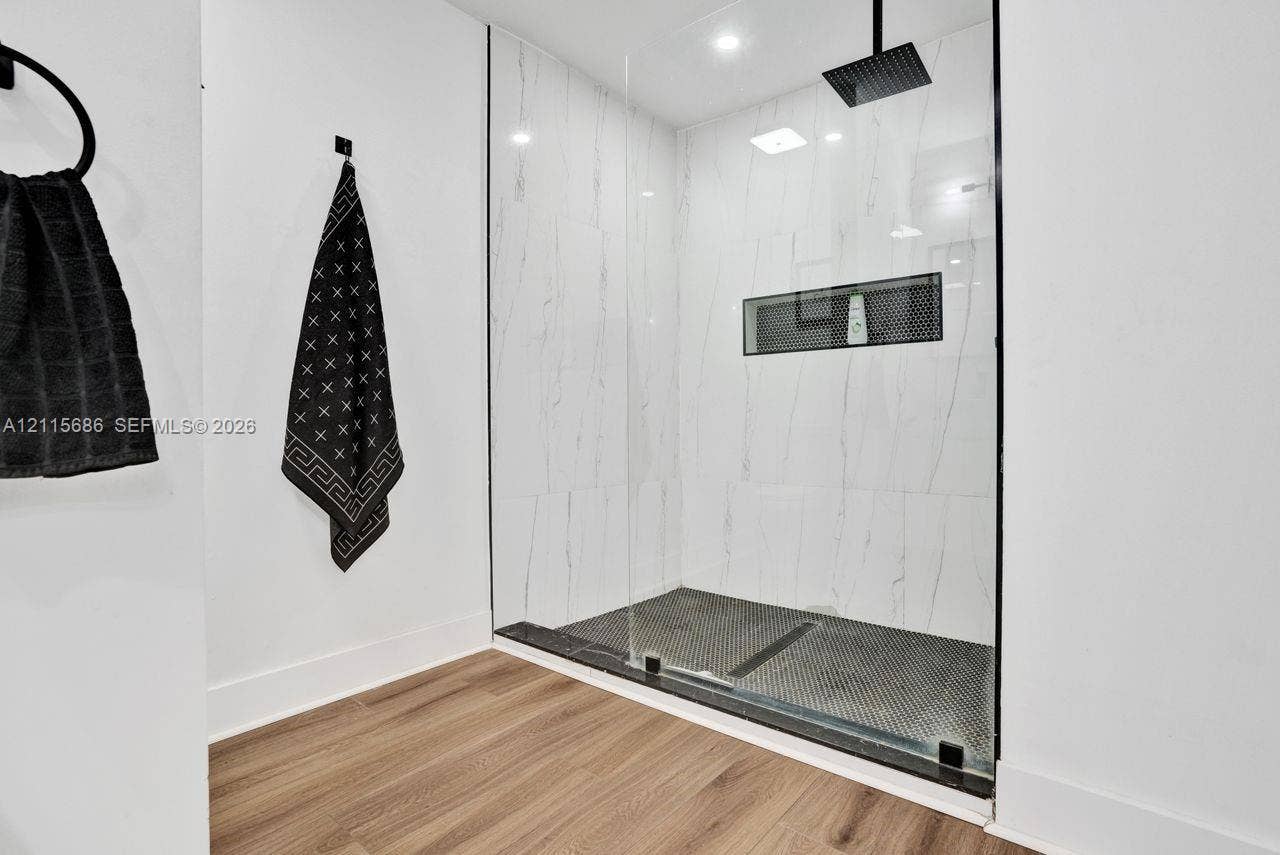 8946 SW 150th Ct Circle E, Miami, Miami, FL 33196 Walk-in shower featuring floor-to-ceiling stone-finish wall tile, frameless glass enclosure, matte black rainfall showerhead, recessed wall niche, and hex-pattern floor tile