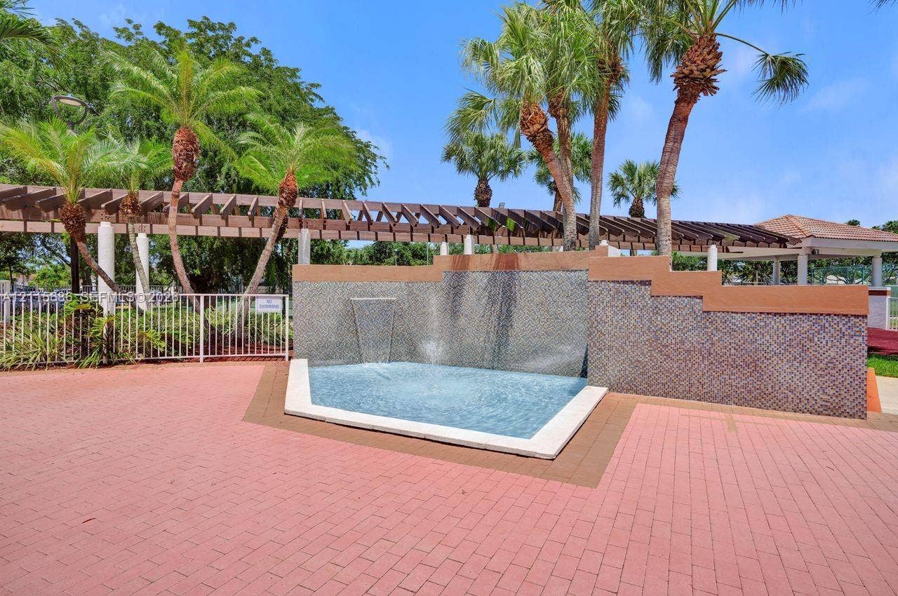 8946 SW 150th Ct Circle E, Miami, Miami, FL 33196 Exterior water feature with tiered stone wall and fountain, paved brick patio, wood-beam pergola, and mature palm trees
