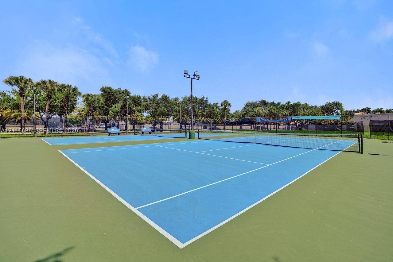 8946 SW 150th Ct Circle E, Miami, Miami, FL 33196 Dual tennis courts featuring a synthetic surface, perimeter chain-link fencing, integrated lighting poles, and mature tree landscaping