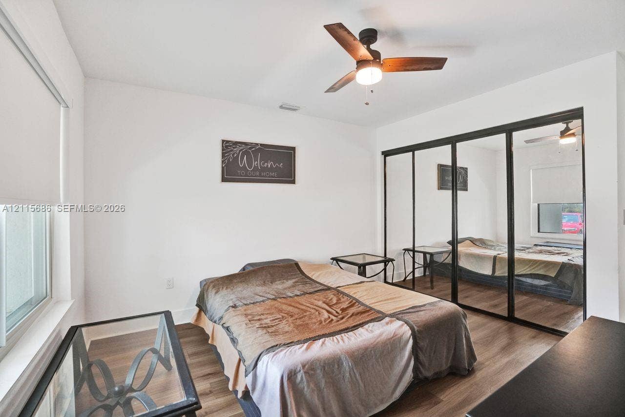 8946 SW 150th Ct Circle E, Miami, Miami, FL 33196 Wood-finish flooring, sliding mirror-paneled closet doors with black frames, modern ceiling fan with integrated lighting, and roller window shades
