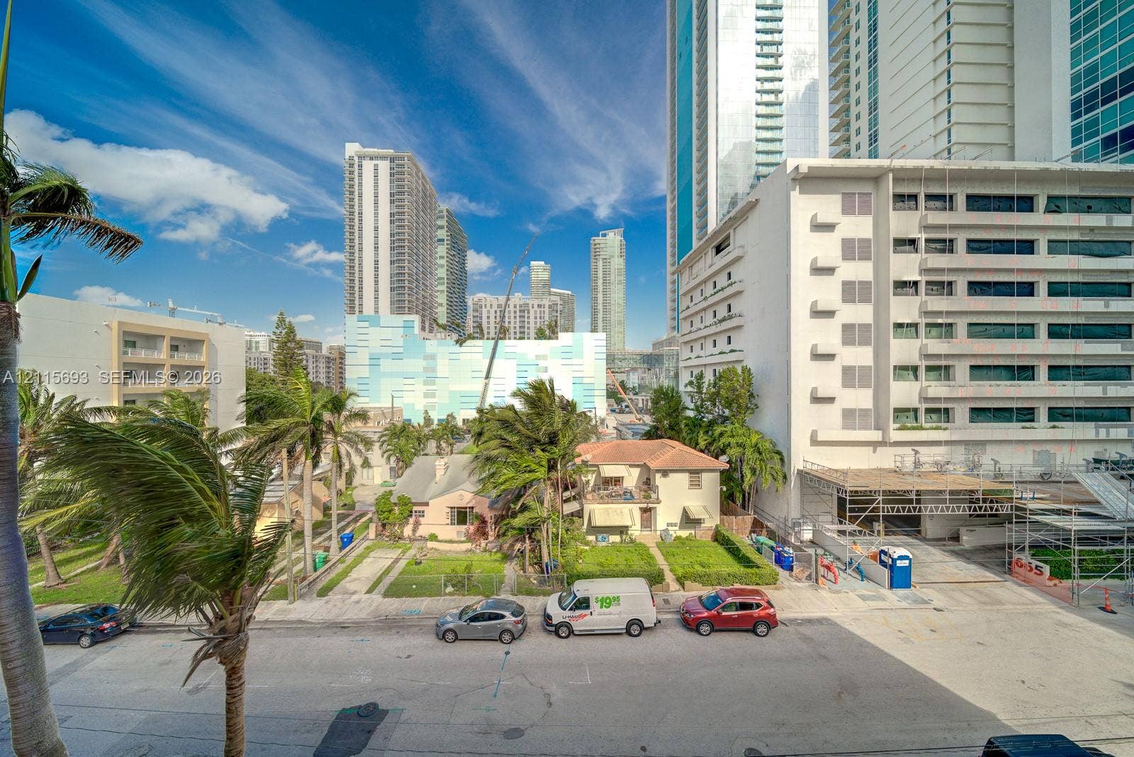 Urban streetscape featuring mid-rise architecture, mature palm trees, and clear blue sky