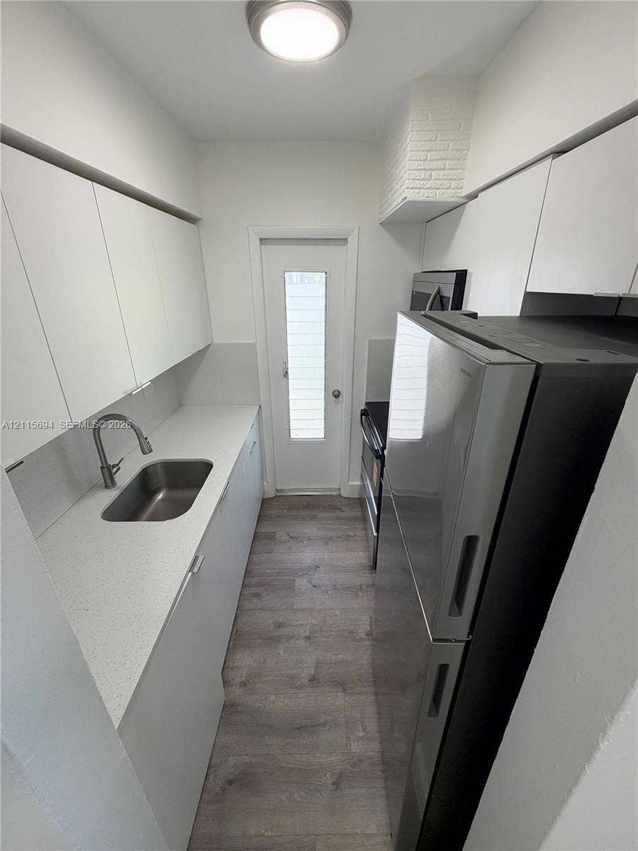 619 SW 7th Avenue, #7, Miami, Miami, FL 33130 Galley kitchen featuring flat-panel white cabinetry, solid surface countertops, stainless steel sink with pull-down faucet, wood-finish flooring, and a glass-paneled exterior door