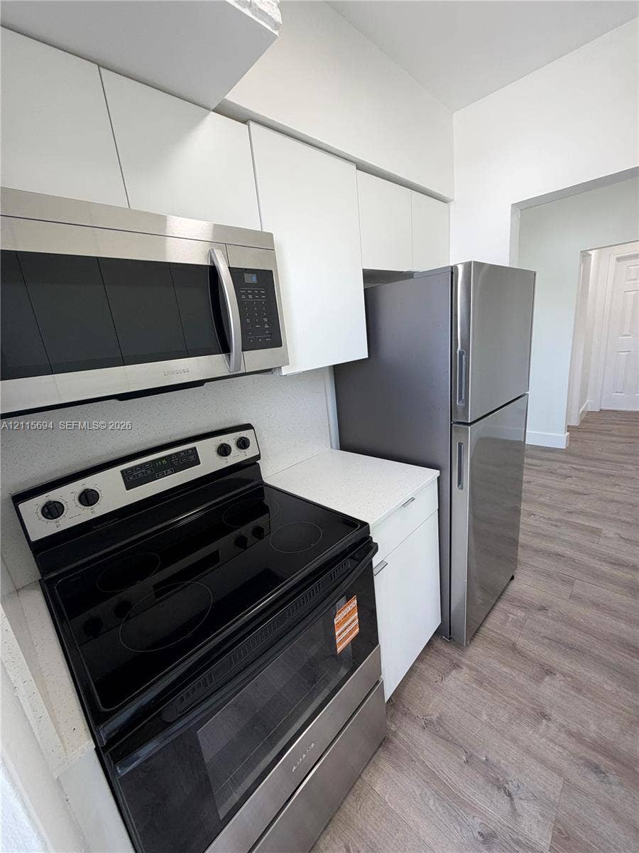 619 SW 7th Avenue, #7, Miami, Miami, FL 33130 Kitchen featuring white flat-panel cabinetry, stainless steel microwave, glass-top range, stainless steel refrigerator, and wood-finish flooring