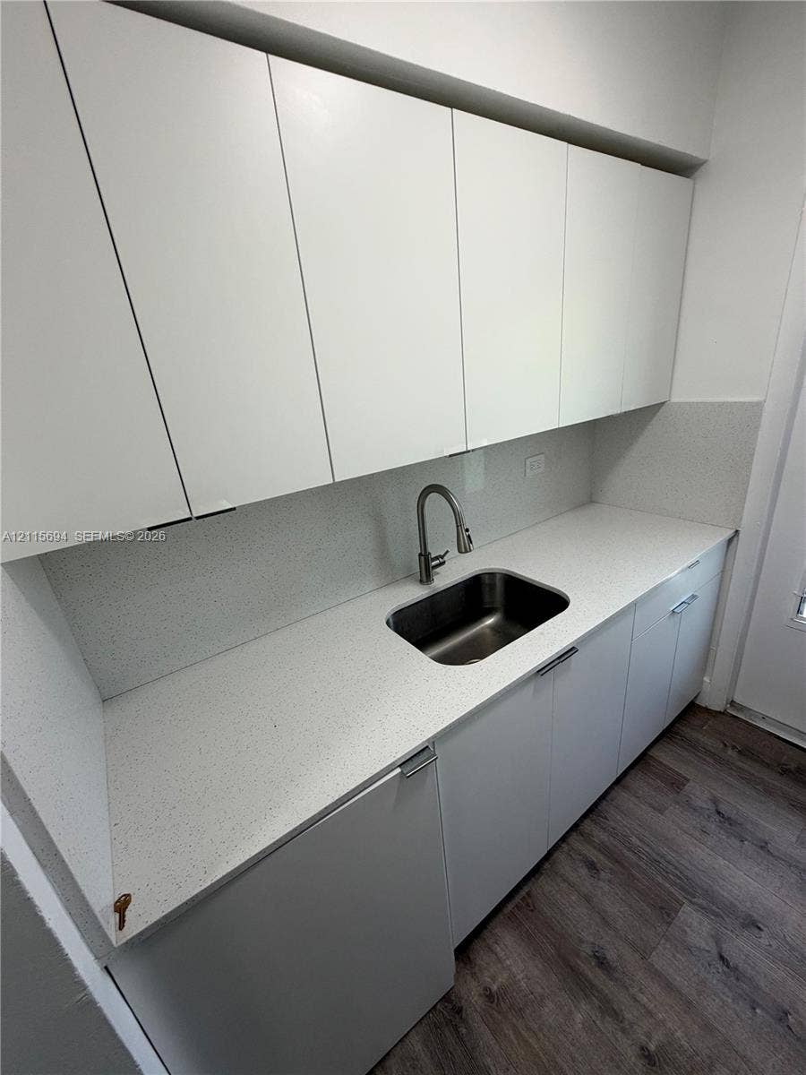 619 SW 7th Avenue, #7, Miami, Miami, FL 33130 Minimalist kitchen featuring flat-panel white cabinetry, speckled composite countertop, stainless steel undermount sink with arched faucet, and wood-finish flooring