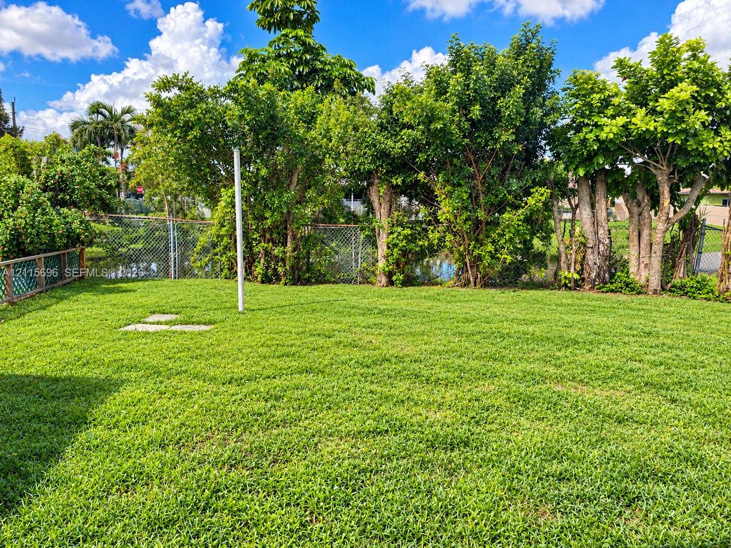 1101 NW 55th Avenue, #B, Lauderhill, Lauderhill, FL 33313 Expansive backyard featuring a level lawn, mature trees, chain-link fencing, and stone hardscaping elements
