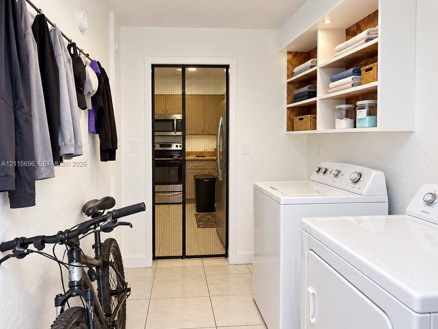 1101 NW 55th Avenue, #B, Lauderhill, Lauderhill, FL 33313 Laundry room featuring white tile flooring, built-in wall shelving with integrated recessed lighting, and a metal garment hanging rod