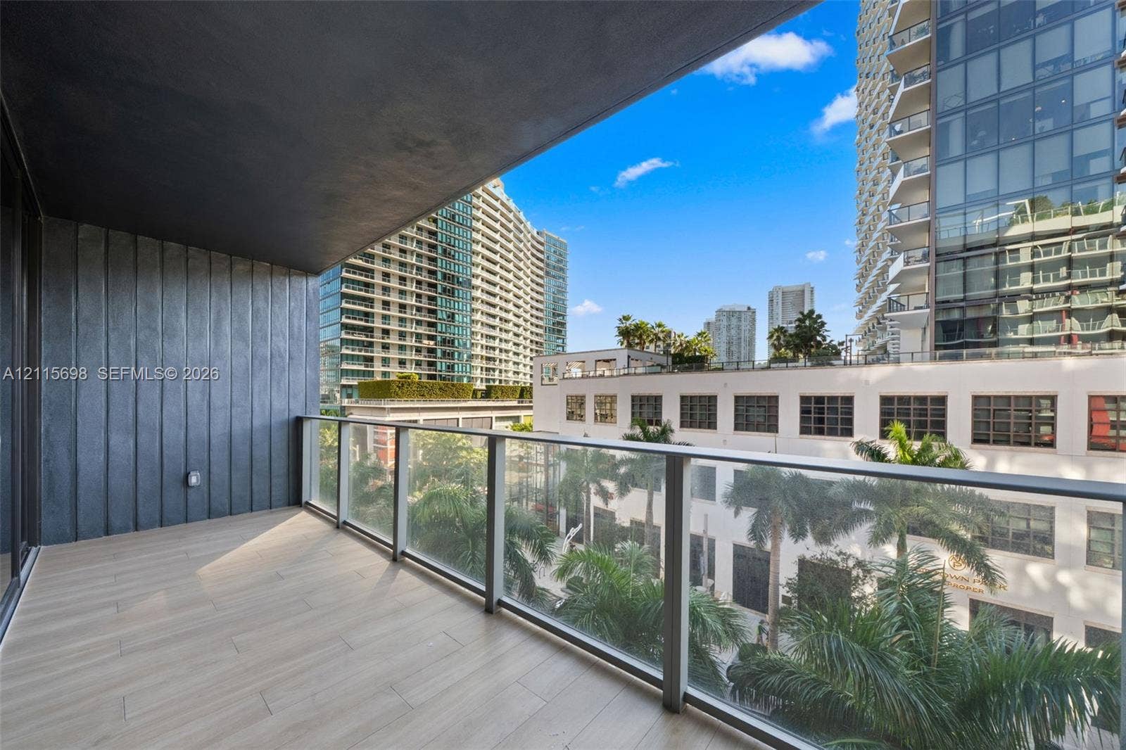 Covered balcony featuring wood-finish flooring, vertical panel siding, and a glass-paneled railing