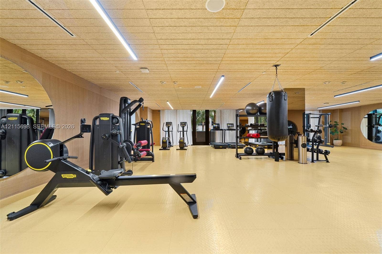 Fitness space featuring wood-panel wall cladding, textured acoustic ceiling panels, wall-to-wall integrated mirrors, and recessed linear lighting