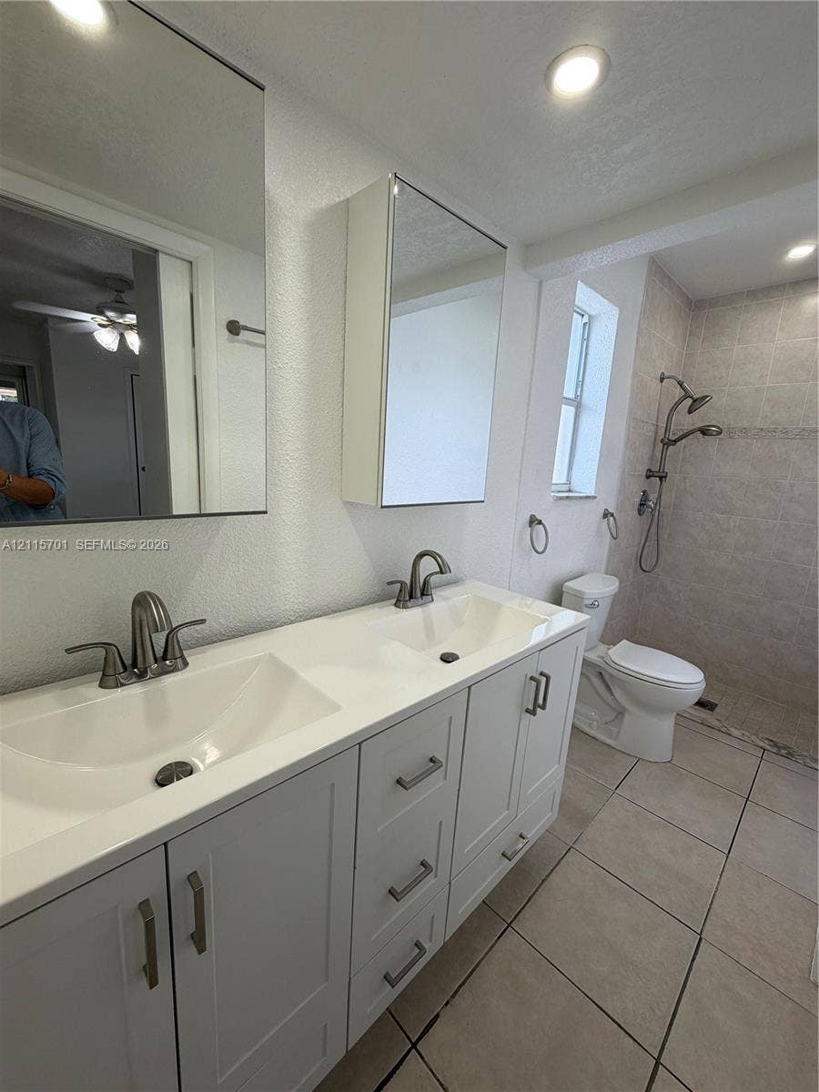 8641 NW 25th Court, #864, Sunrise, Sunrise, FL 33322 Dual-sink vanity with white cabinetry, light-toned solid surface countertop, rectangular under-mount sinks, mirrored medicine cabinets, and walk-in shower with adjustable showerhead