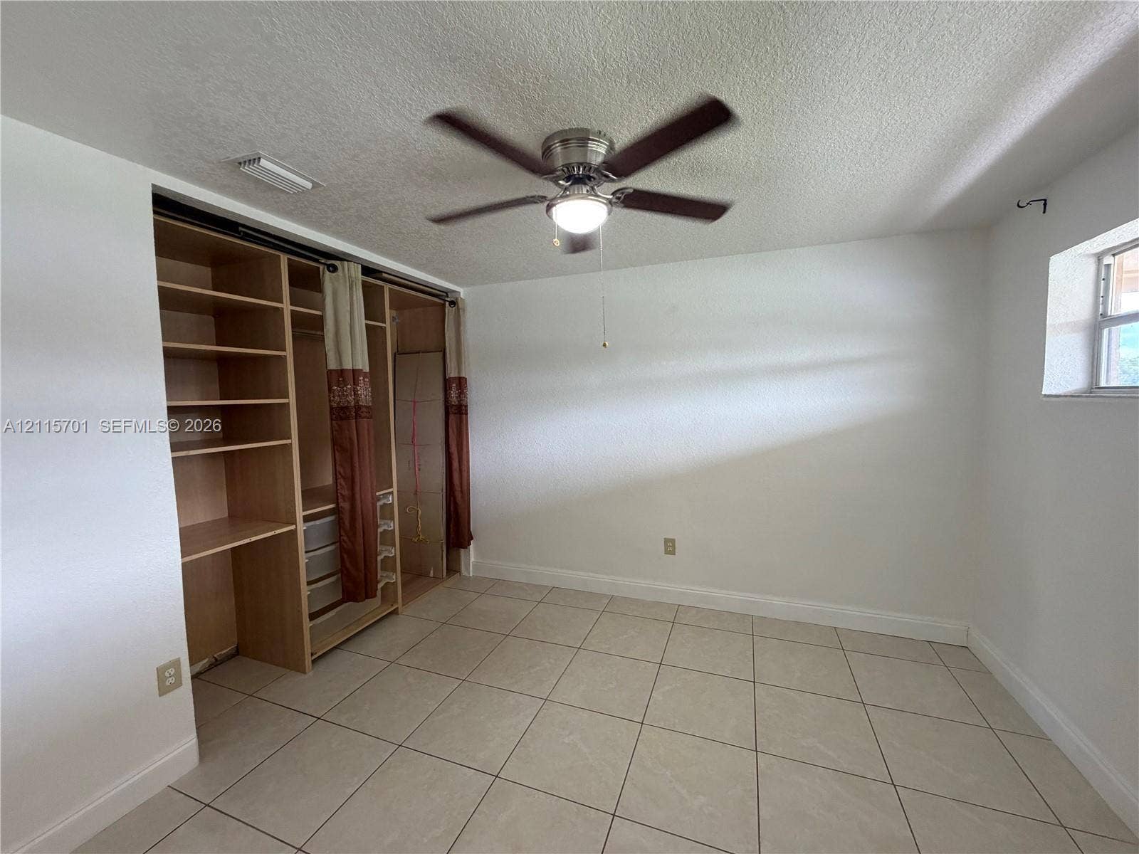 8641 NW 25th Court, #864, Sunrise, Sunrise, FL 33322 Interior room featuring large-format ceramic tile flooring, built-in wooden shelving unit with integrated storage, and a multi-blade ceiling fan with an attached light fixture