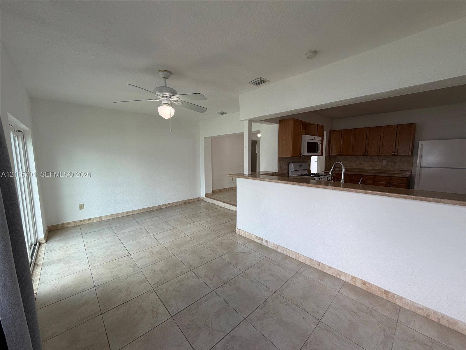 8641 NW 25th Court, #864, Sunrise, Sunrise, FL 33322 Open-concept interior featuring large-format ceramic tile flooring, a breakfast bar with stone-finish countertops, warm-toned wood cabinetry, and a ceiling fan with integrated lighting