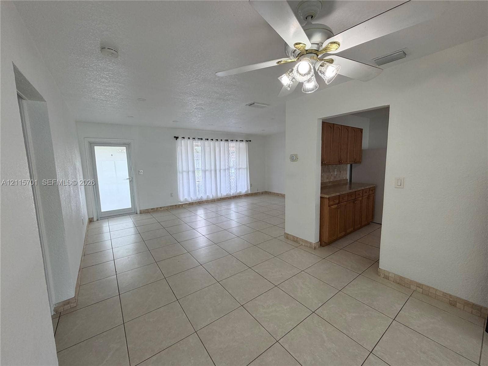 8641 NW 25th Court, #864, Sunrise, Sunrise, FL 33322 Open interior space featuring light-toned tile flooring, white-finish walls, ceiling-mounted paddle fan with integrated light fixture, and wood-finish cabinetry