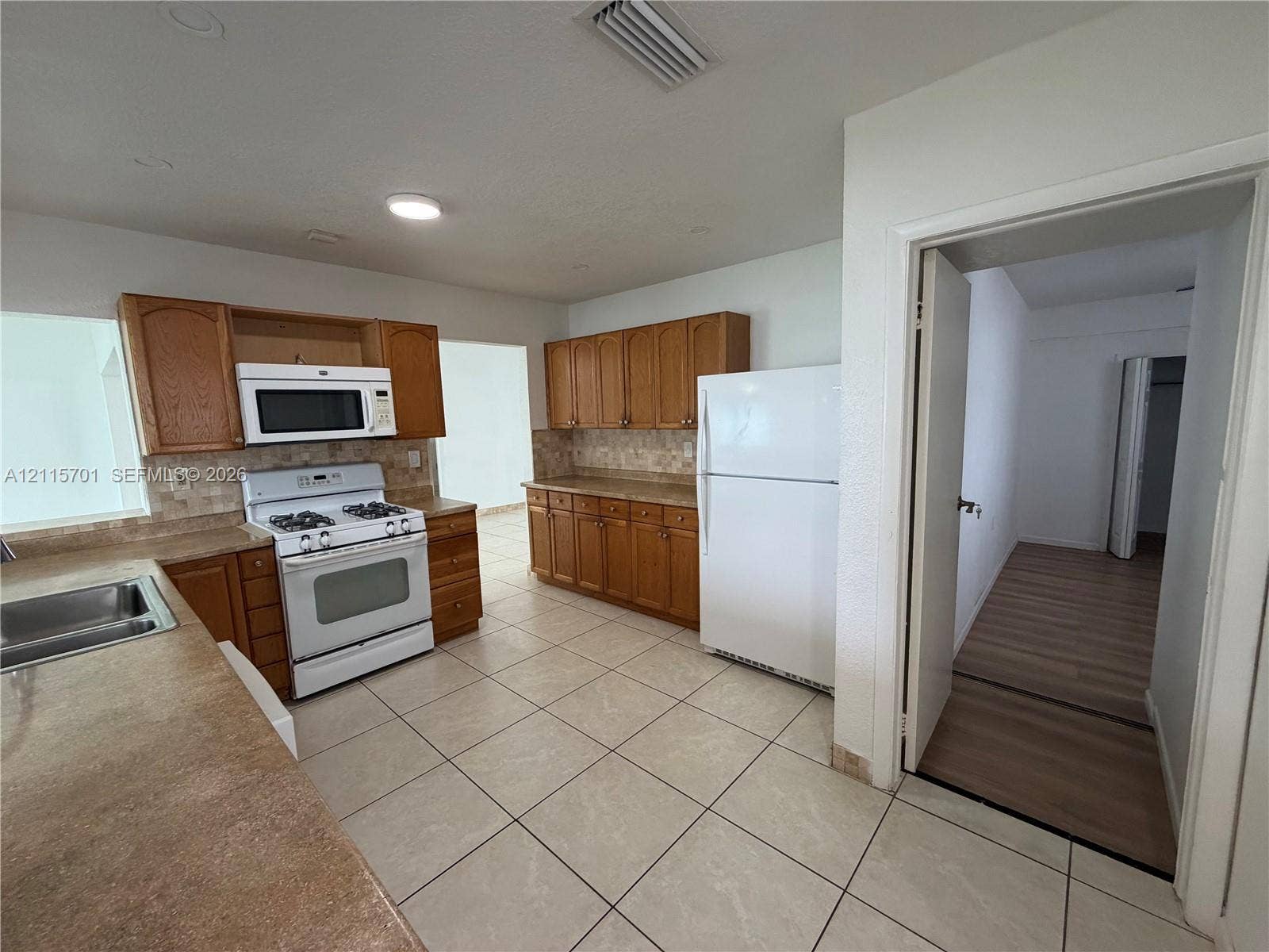 8641 NW 25th Court, #864, Sunrise, Sunrise, FL 33322 Kitchen featuring wood cabinetry, tile flooring, stone-finish countertops, tile backsplash, and white appliance suite