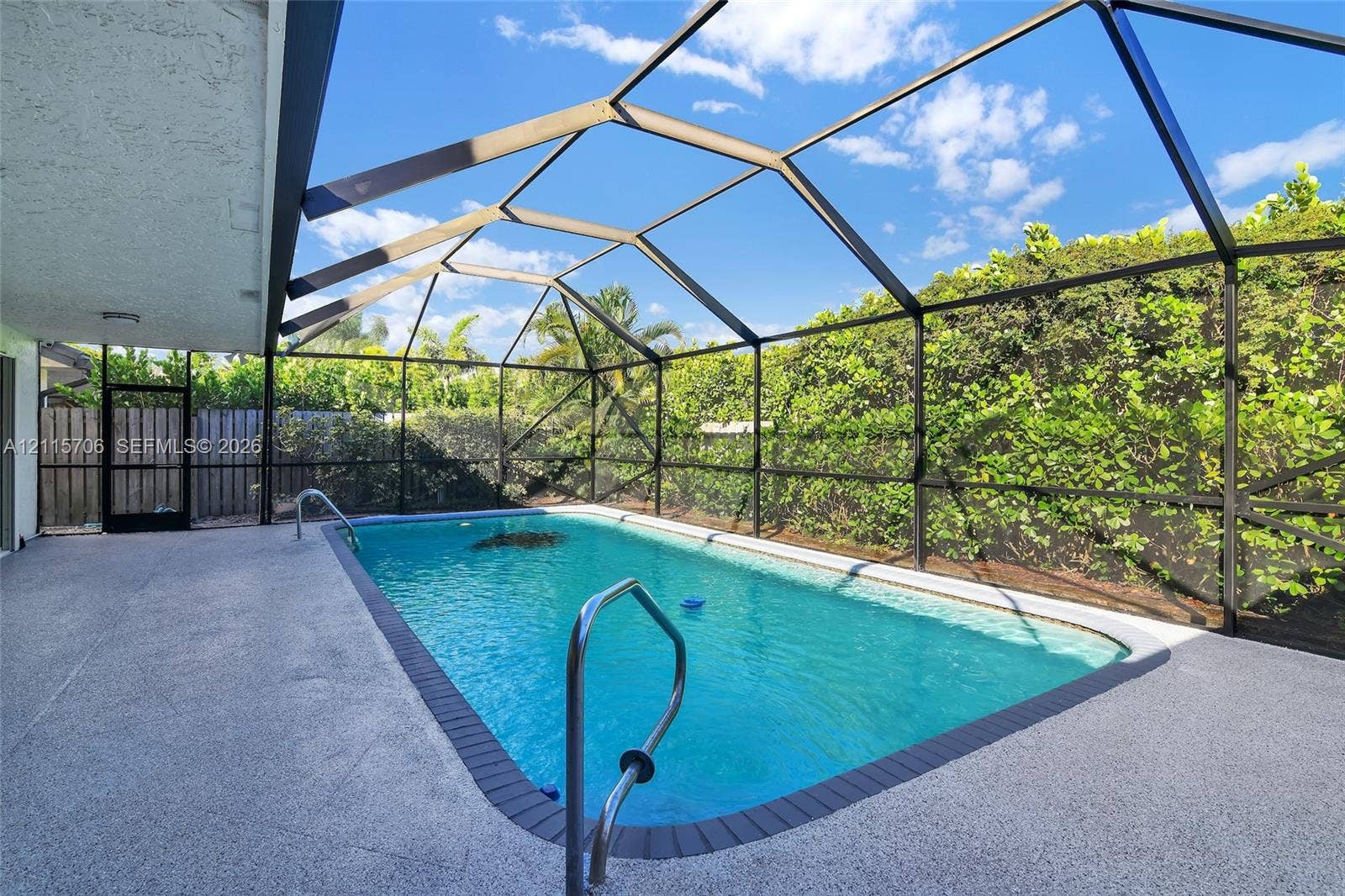 5184 Deerhurst Crescent Circle, Boca Raton, FL 33486 Screen-enclosed swimming pool featuring a textured concrete deck, metal handrails, and surrounding privacy hedges