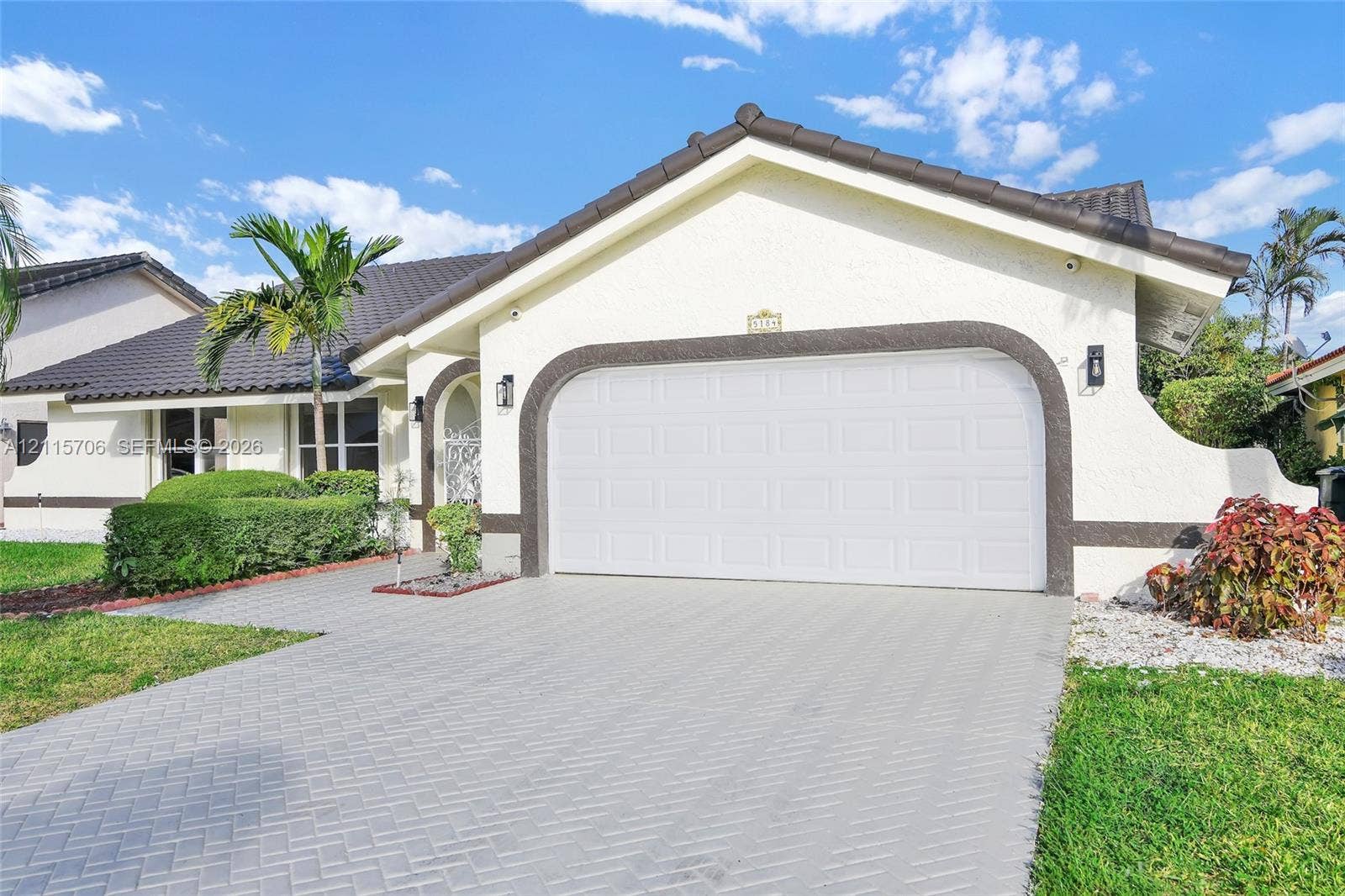 5184 Deerhurst Crescent Circle, Boca Raton, FL 33486 Stucco exterior with decorative arched trim, herringbone-patterned paver driveway, two-car garage, and tiled roof