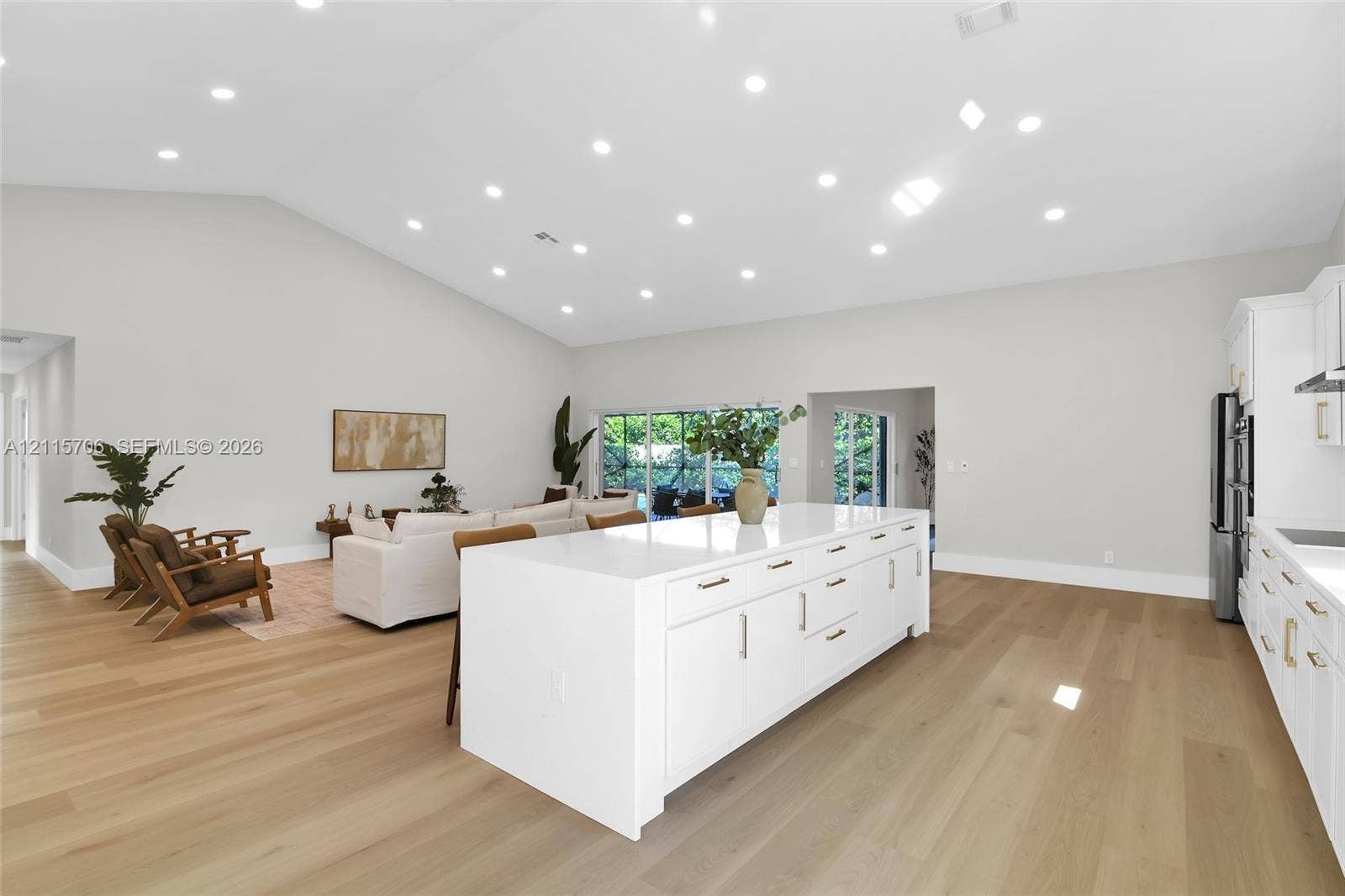 5184 Deerhurst Crescent Circle, Boca Raton, FL 33486 Open-concept interior featuring vaulted ceilings, recessed lighting, wood-finish flooring, a white kitchen island with cabinetry, and large sliding glass doors