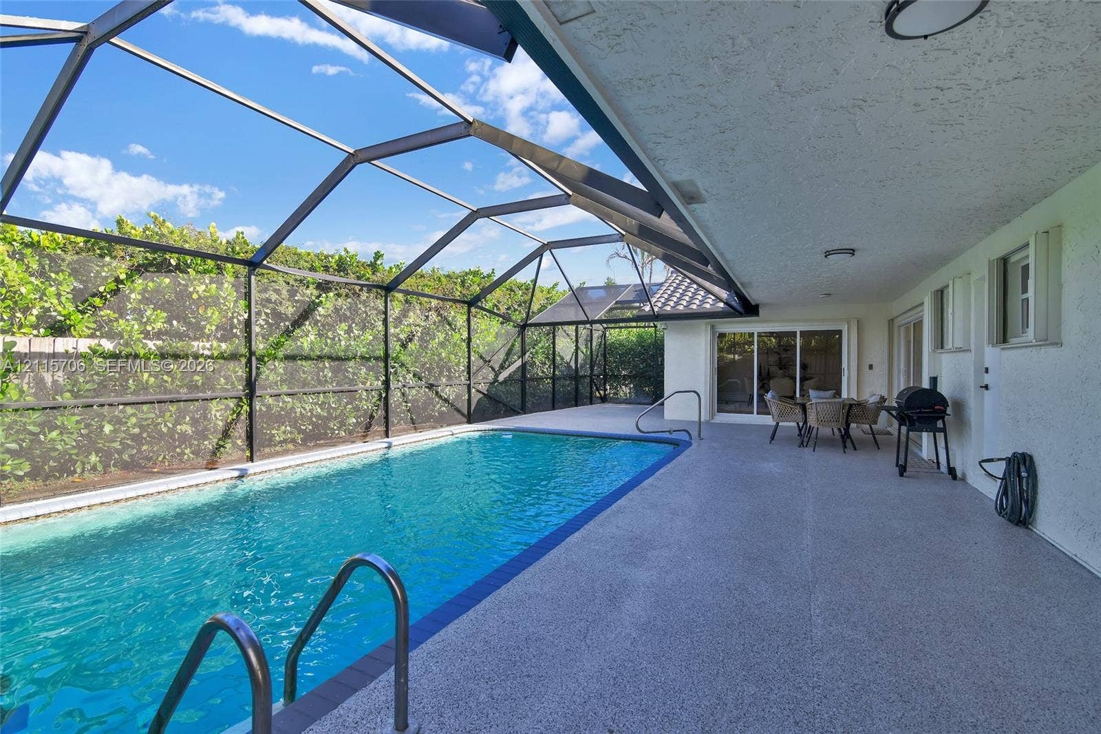 5184 Deerhurst Crescent Circle, Boca Raton, FL 33486 Screened-in outdoor living area featuring a swimming pool with metal ladder, expansive concrete pool deck, and perimeter greenery