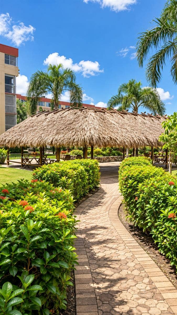 406 NW 68th Avenue, #115, Plantation, Plantation, FL 33317 Outdoor pavilion with a thatched roof, brick-paver pathway, and manicured landscaping featuring mature palm trees and flowering hedges
