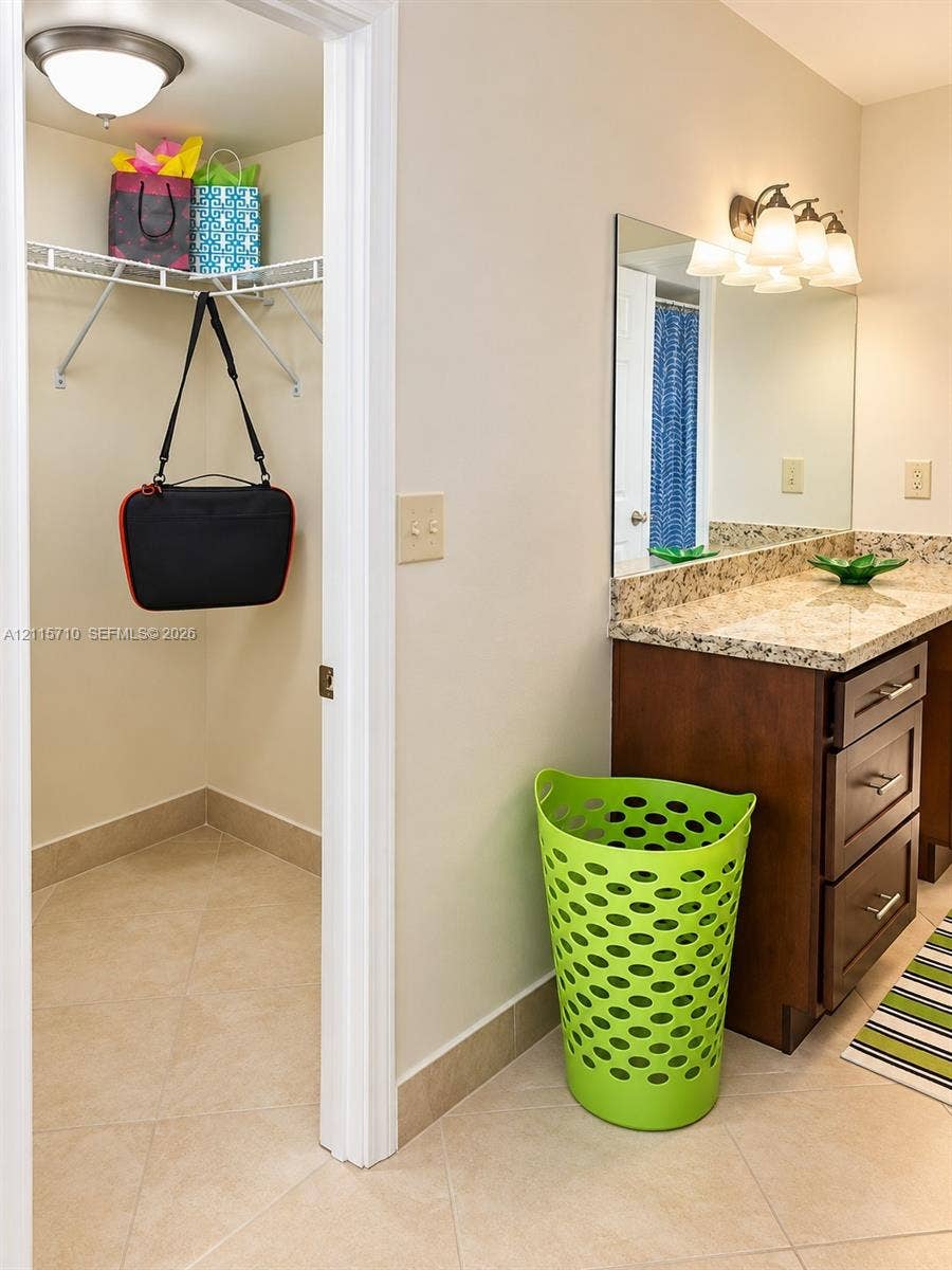 406 NW 68th Avenue, #115, Plantation, Plantation, FL 33317 Bathroom featuring a vanity with dark wood-finish cabinetry, stone-look countertop, large vanity mirror, three-light fixture, and an internal walk-in closet with wire shelving