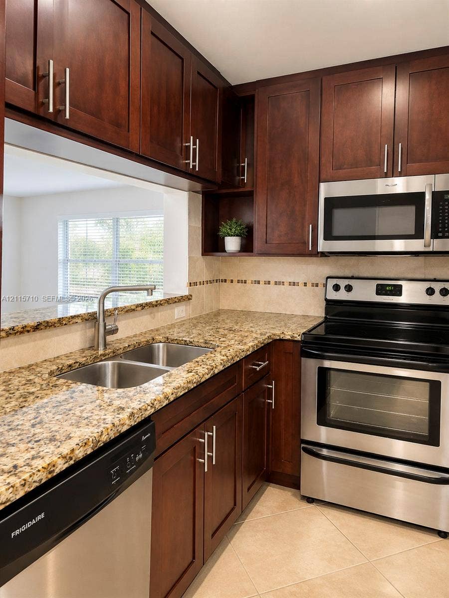 406 NW 68th Avenue, #115, Plantation, Plantation, FL 33317 Kitchen featuring dark-toned cabinetry, stone-finish countertops, stainless steel appliances, ceramic tile backsplash, and a double-basin undermount sink