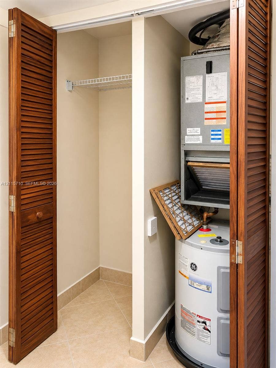 406 NW 68th Avenue, #115, Plantation, Plantation, FL 33317 Utility closet featuring wood-finish louvered bi-fold doors, tile flooring, built-in wire shelving, and a dedicated housing for the water heater and HVAC air handler unit