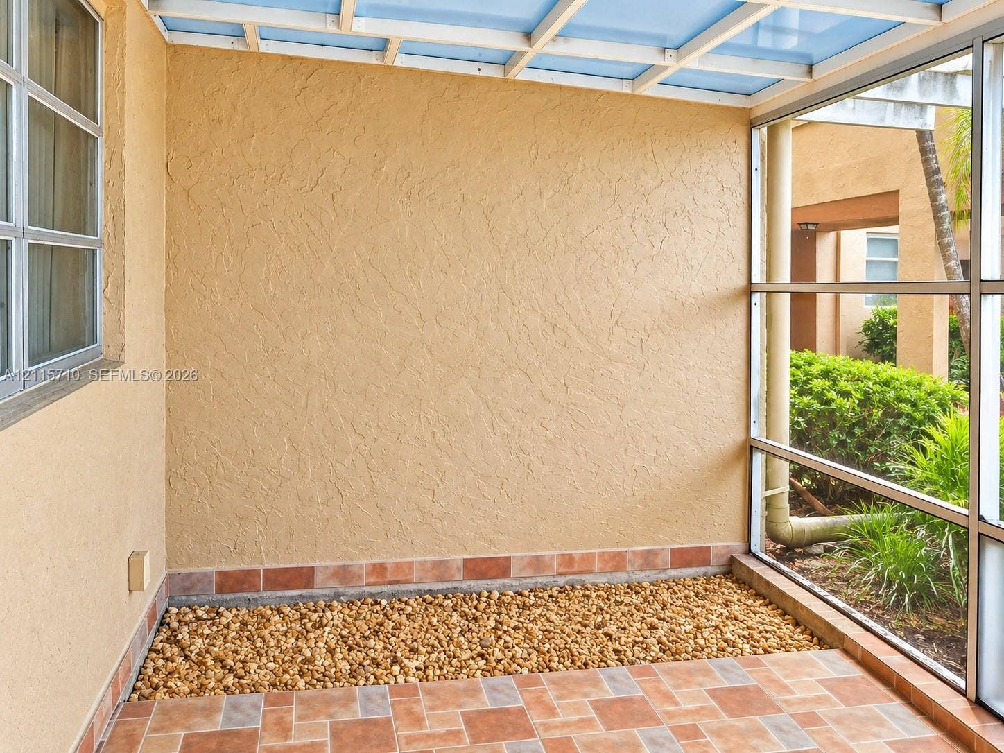 406 NW 68th Avenue, #115, Plantation, Plantation, FL 33317 Screened patio featuring a textured stucco finish, multi-tonal ceramic tile flooring, a built-in gravel border, and a translucent roof panel system