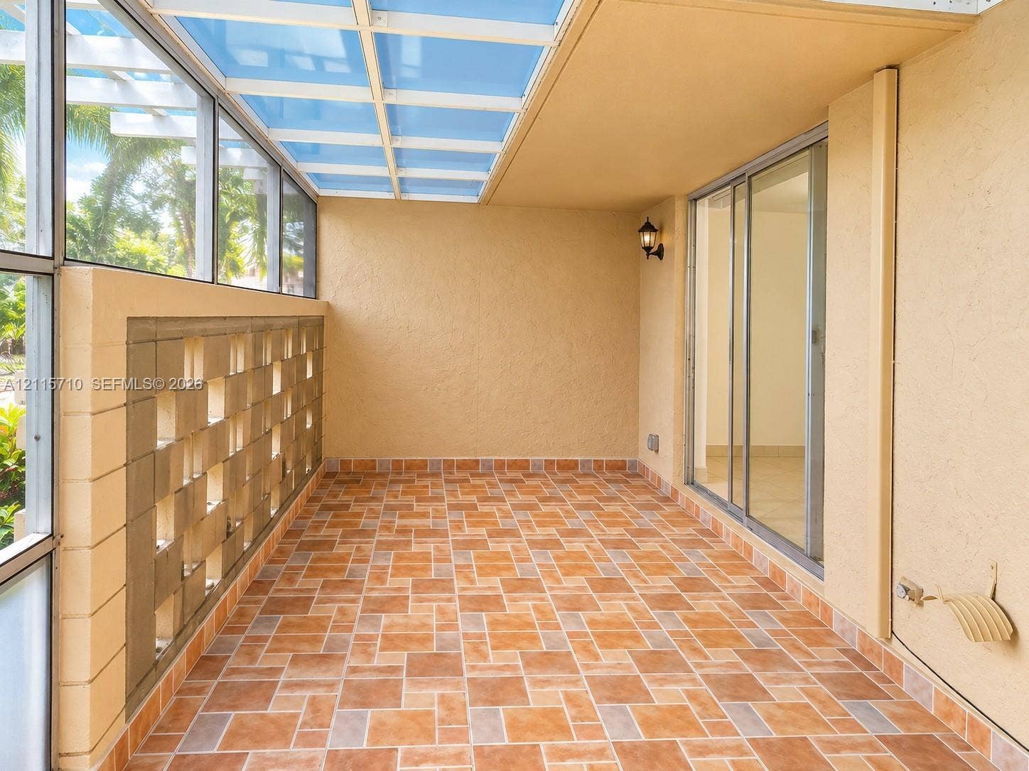 406 NW 68th Avenue, #115, Plantation, Plantation, FL 33317 Enclosed patio featuring a translucent roof panel, decorative concrete block wall, patterned ceramic tile flooring, and sliding glass door entry