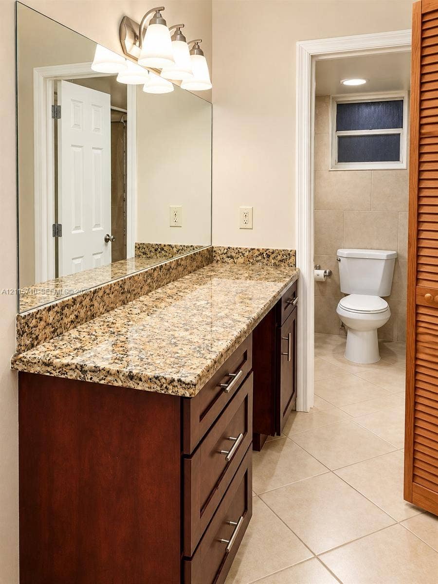 406 NW 68th Avenue, #115, Plantation, Plantation, FL 33317 Vanity featuring stone-finish countertop, dark wood-finish cabinetry with brushed metal hardware, large wall-mounted mirror, multi-light fixture, and ceramic tile flooring