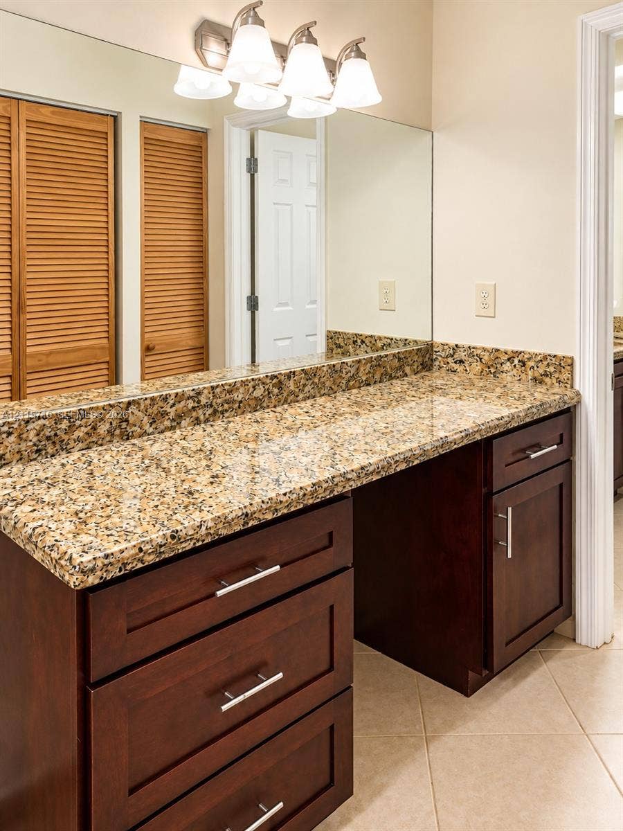 406 NW 68th Avenue, #115, Plantation, Plantation, FL 33317 Vanity featuring dark wood-finish cabinetry, stone countertop, full-width mirror, brushed metal hardware, and multi-bulb light fixture