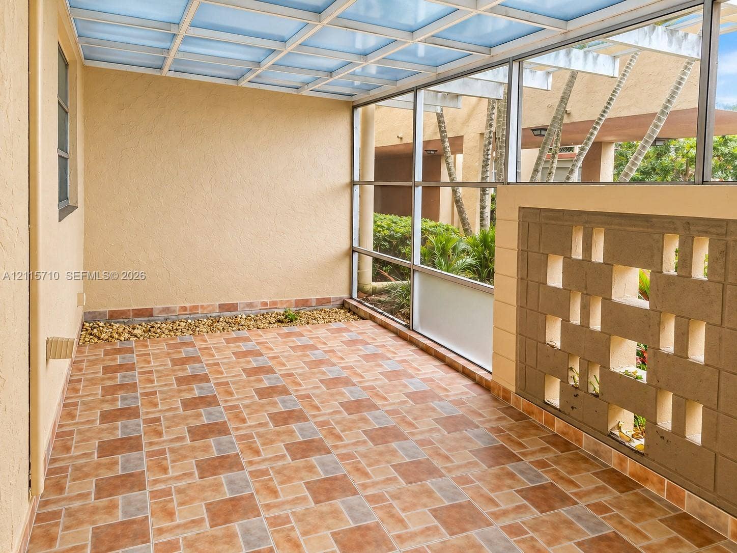 406 NW 68th Avenue, #115, Plantation, Plantation, FL 33317 Screened-in patio featuring patterned tile flooring, a translucent roof structure, decorative masonry screen wall, and a stone-lined planter border