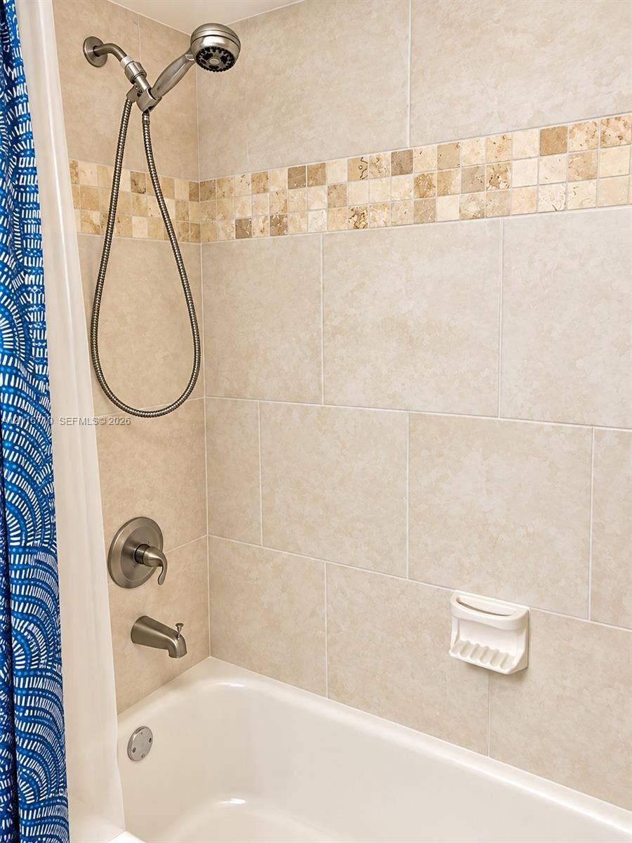 406 NW 68th Avenue, #115, Plantation, Plantation, FL 33317 Shower and tub combination featuring large-format neutral tile surround, integrated stone mosaic accent border, satin nickel plumbing fixtures, and a built-in soap dish
