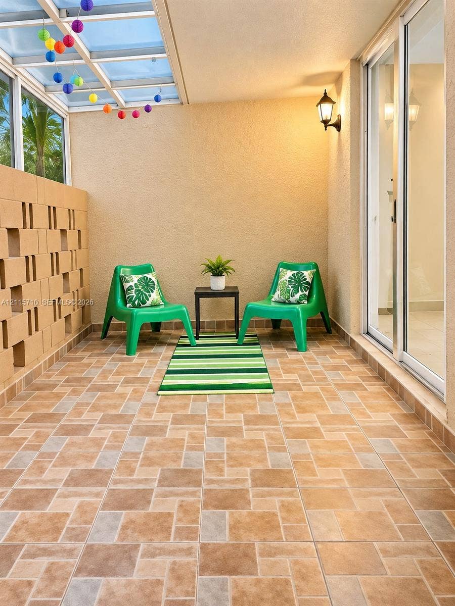 406 NW 68th Avenue, #115, Plantation, Plantation, FL 33317 Covered patio featuring ceramic tile flooring, a geometric breeze block wall, a glass-paneled roof system, and wall-mounted exterior lighting