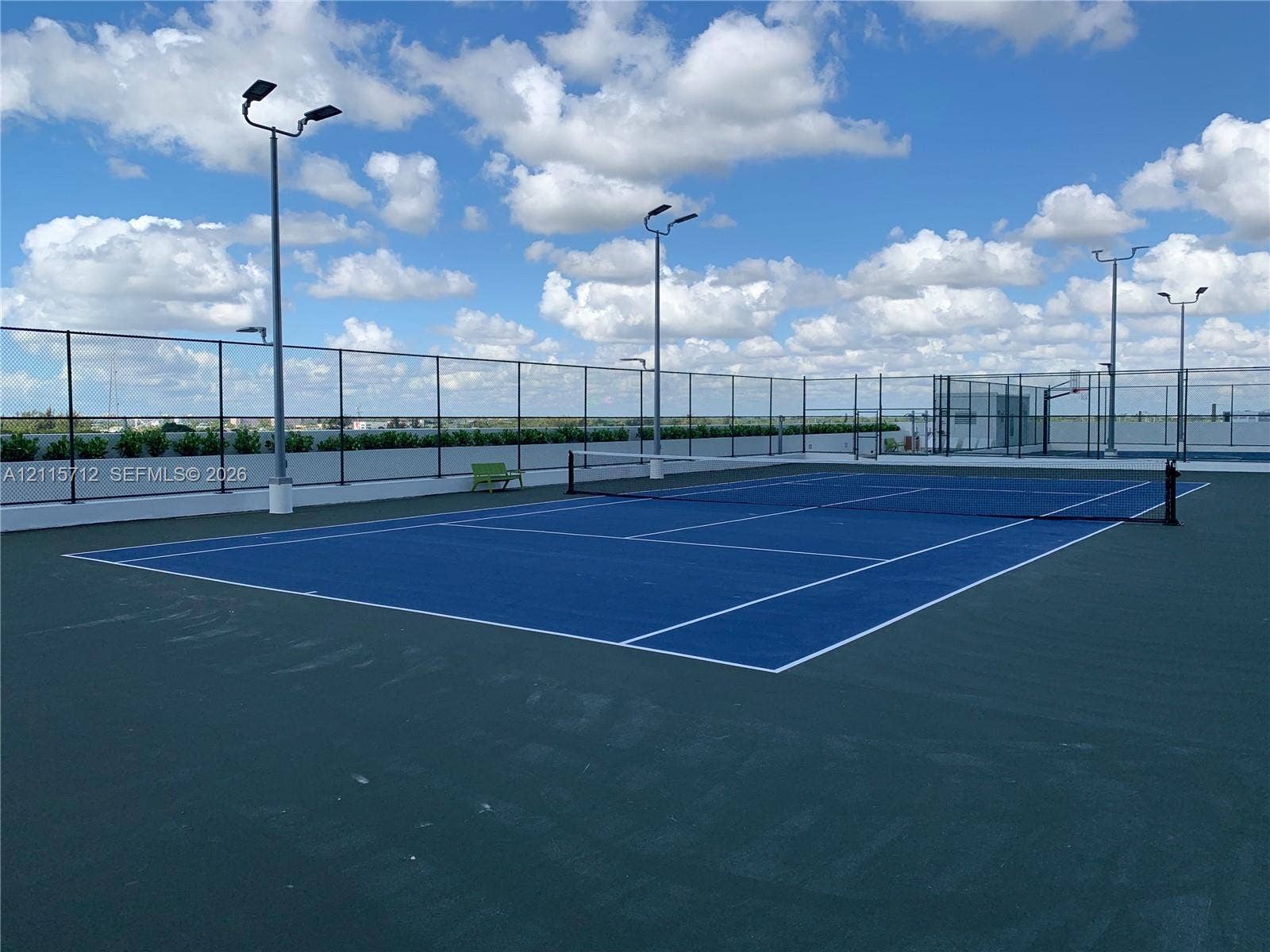 16385 Biscayne Boulevard, #1906, North Miami Beach, North Miami Beach, FL 33160 Rooftop tennis court featuring a blue surface with white court markings, perimeter chain-link fencing, and integrated pole-mounted floodlighting