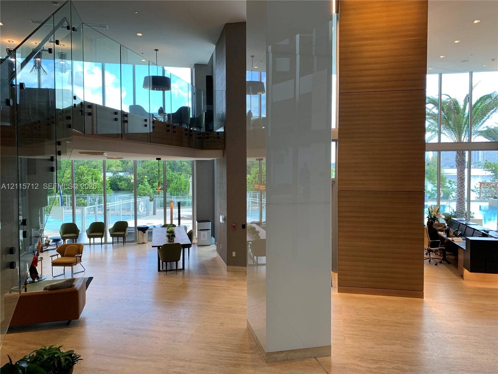 16385 Biscayne Boulevard, #1906, North Miami Beach, North Miami Beach, FL 33160 Double-height interior featuring floor-to-ceiling glass walls, glass-panel staircase railing, wood-finish flooring, and wood-paneled accent wall
