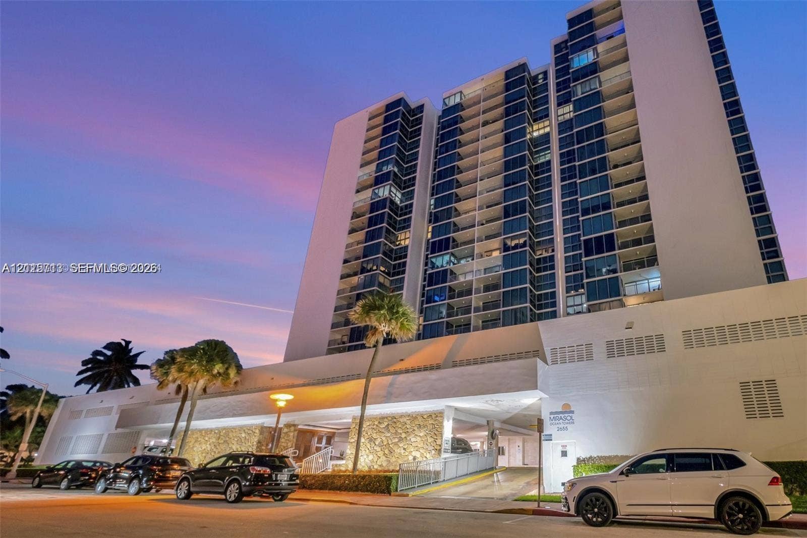 2655 Collins Avenue, #1006, Miami Beach, Miami Beach, FL 33140 High-rise residential exterior featuring expansive glass paneling, recessed private balconies, stone veneer podium cladding, and integrated ground-level parking