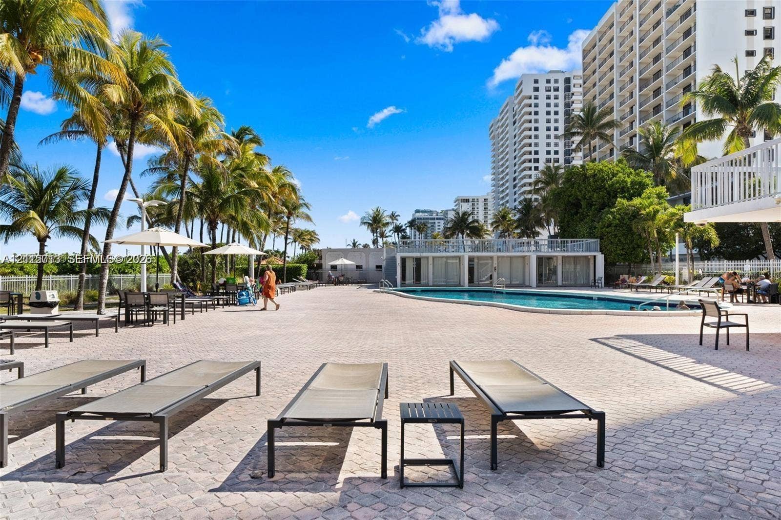 2655 Collins Avenue, #1006, Miami Beach, Miami Beach, FL 33140 Outdoor pool area featuring a paved sun deck, mature palm trees, and a structure with floor-to-ceiling windows