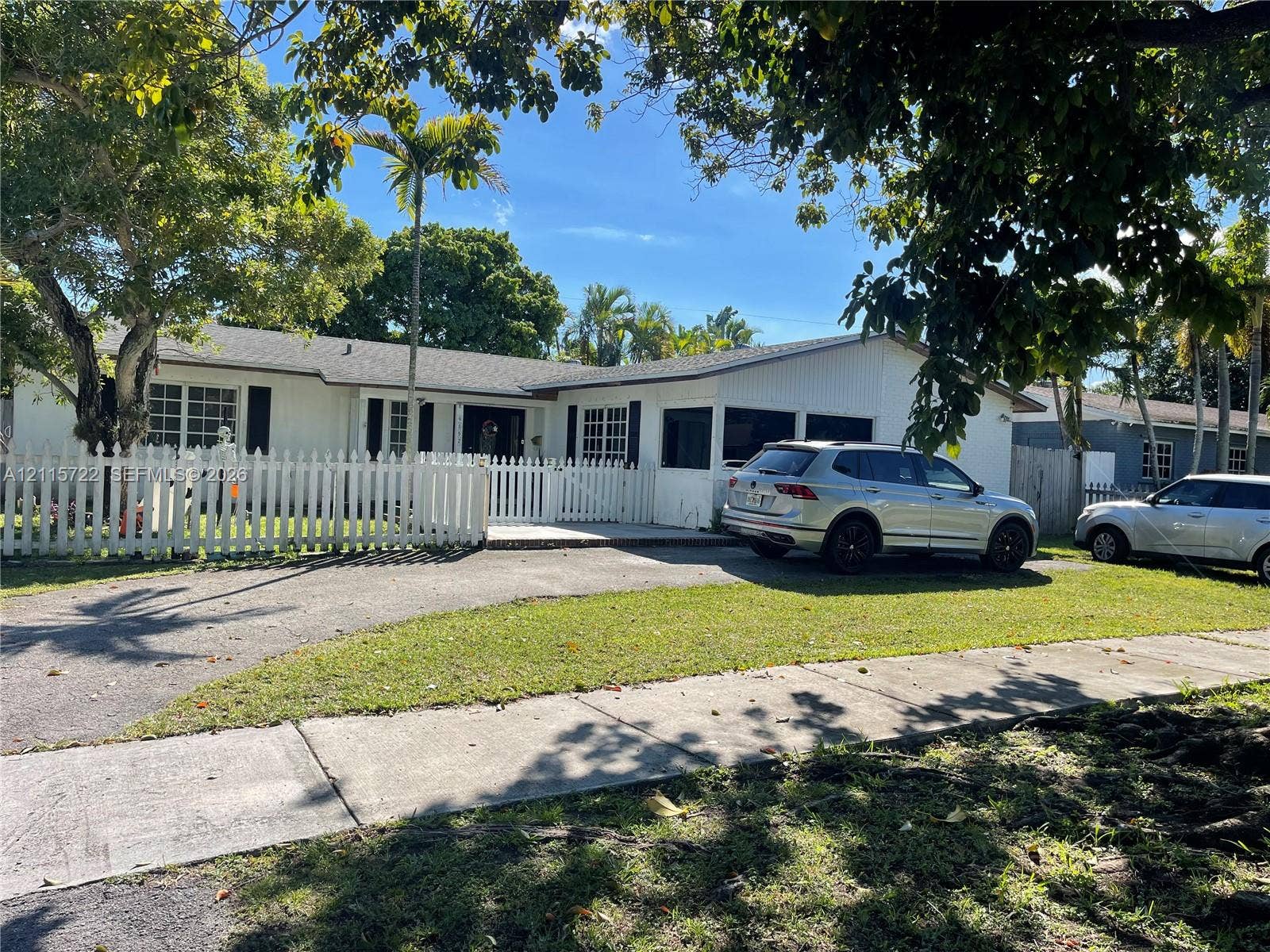 9852 SW 196th Street, Cutler Bay, FL 33157 Single-story exterior featuring white vertical siding, a picket fence perimeter, asphalt-paved driveway, and a screened-in porch