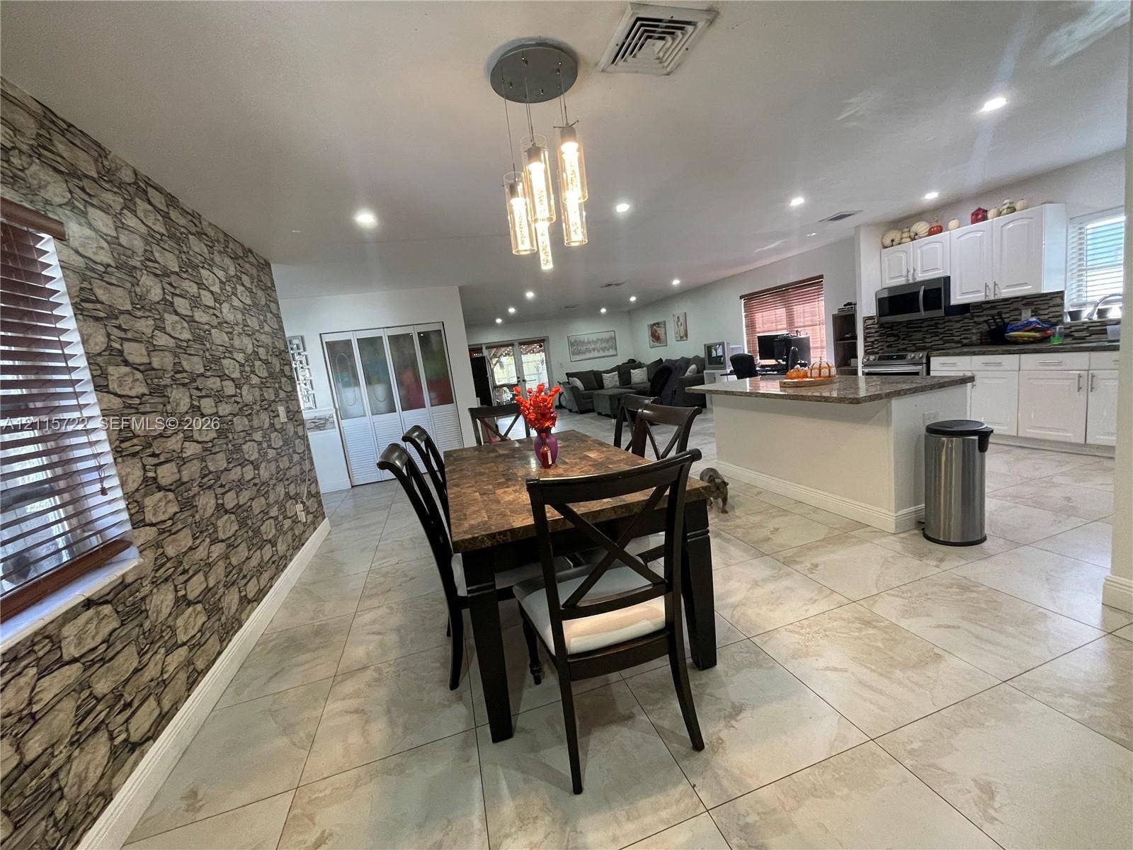 9852 SW 196th Street, Cutler Bay, FL 33157 Stone-textured accent wall, tile flooring, kitchen island with a stone-finish countertop, white shaker-style cabinetry, and a multi-pendant light fixture