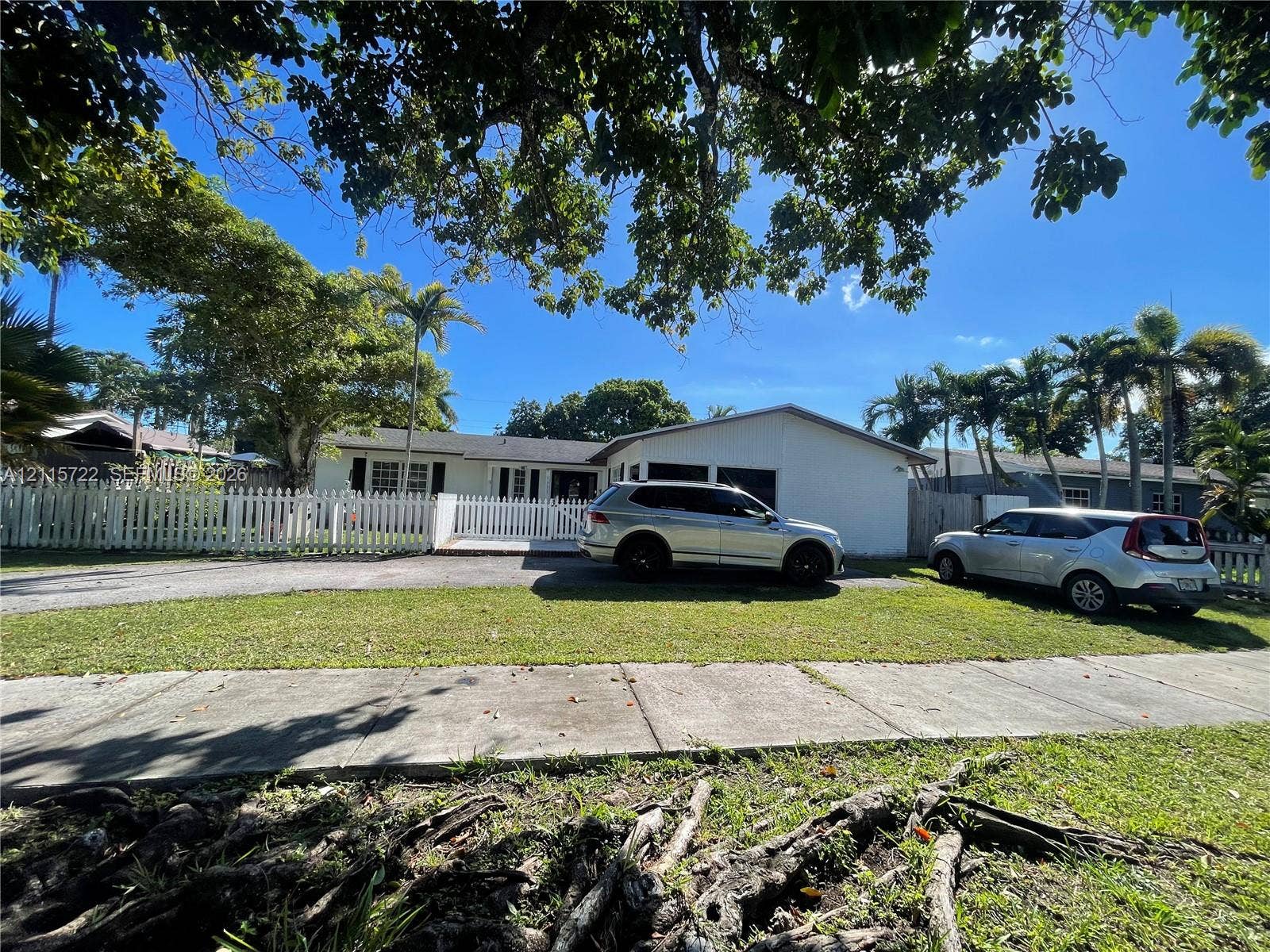 9852 SW 196th Street, Cutler Bay, FL 33157 Single-story residence featuring white exterior siding, a multi-car garage, white picket fencing, and mature canopy trees