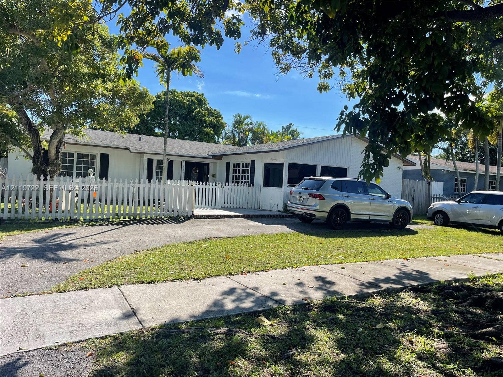 9852 SW 196th Street, Cutler Bay, FL 33157 Single-story residence featuring a white exterior, picket fencing, mature shade trees, and a screened-in porch area