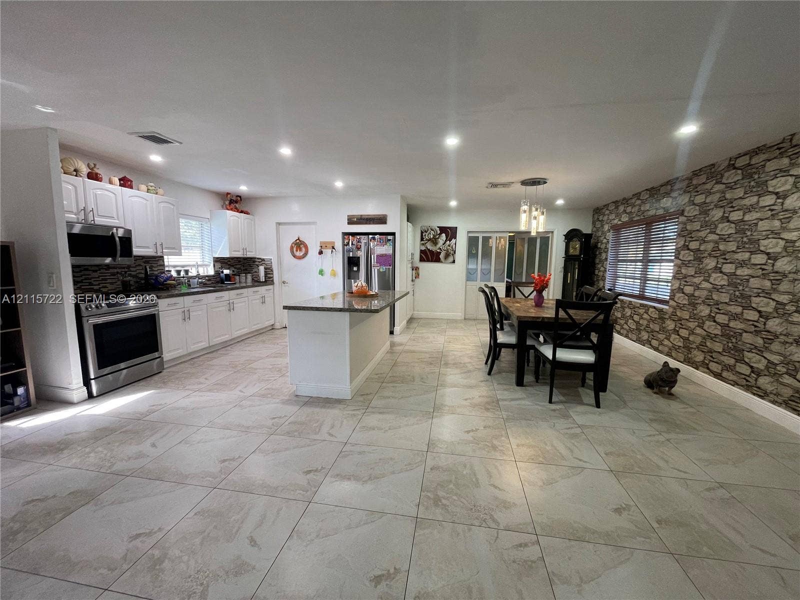 9852 SW 196th Street, Cutler Bay, FL 33157 Kitchen featuring white cabinetry, stone-finish kitchen island, stainless steel appliances, large-format tile flooring, and stone-veneer accent wall