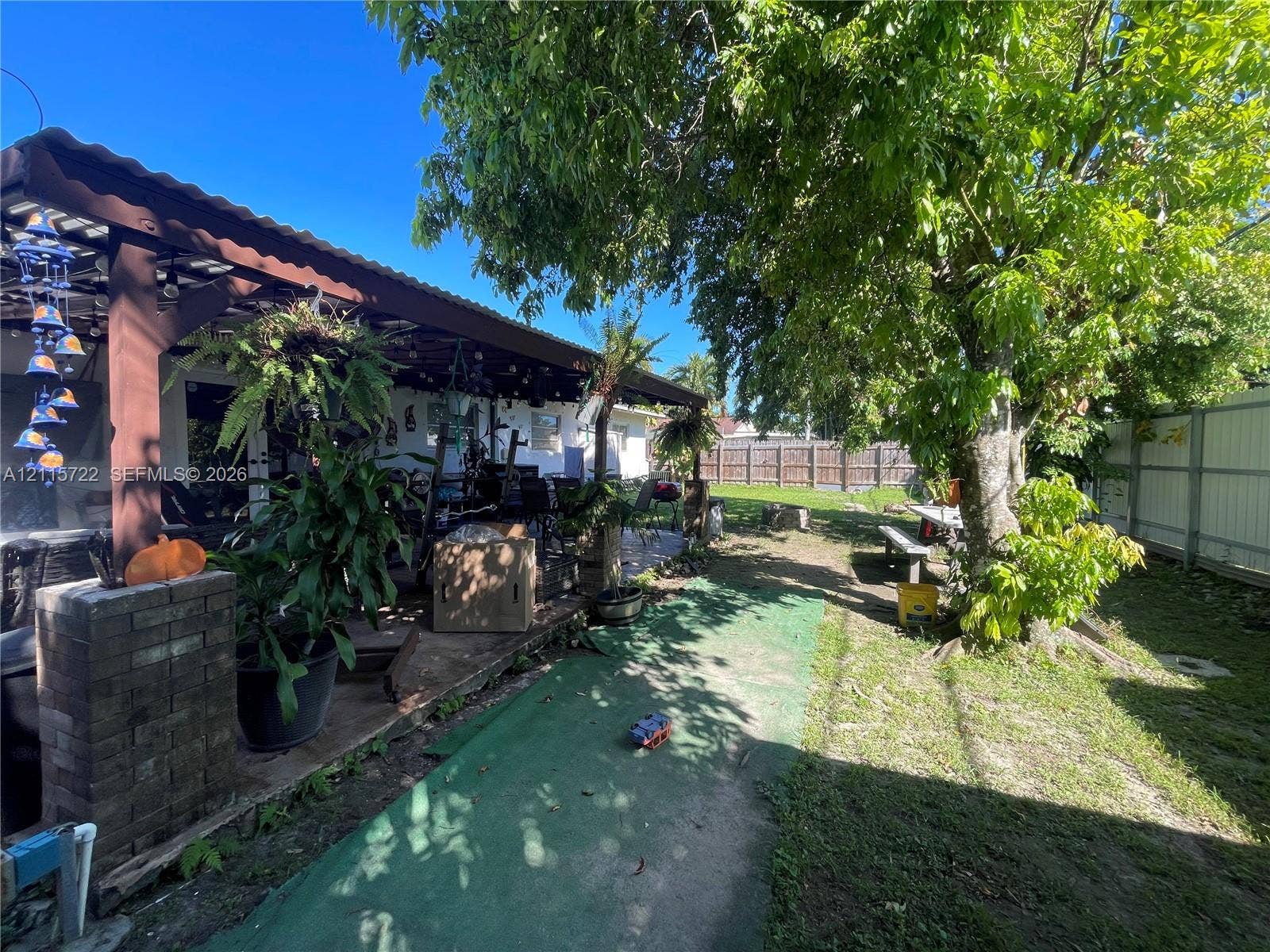 9852 SW 196th Street, Cutler Bay, FL 33157 Covered patio featuring a timber-frame structure and brick masonry pillar, situated within a backyard defined by mature trees and perimeter wood fencing
