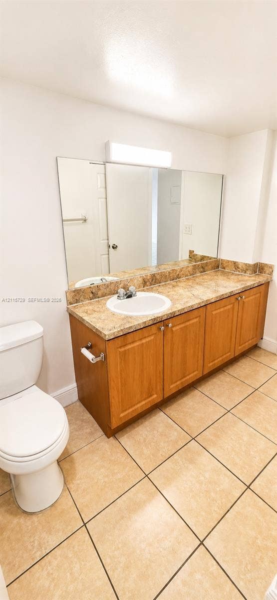 11110 SW 196th Street, #212, Cutler Bay, Cutler Bay, FL 33157 Vanity featuring a stone-pattern countertop, integrated round sink, wooden cabinetry, large wall-mounted mirror, and ceramic tile flooring