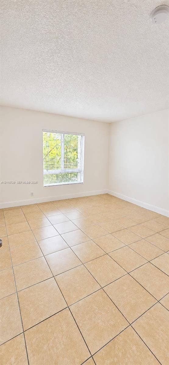 11110 SW 196th Street, #212, Cutler Bay, Cutler Bay, FL 33157 Interior room featuring large-format neutral floor tiling, a single-hung window with horizontal blinds, and a textured ceiling finish