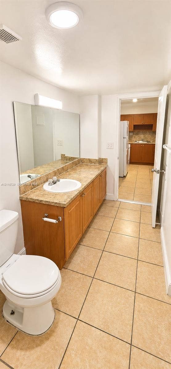 11110 SW 196th Street, #212, Cutler Bay, Cutler Bay, FL 33157 Bathroom featuring a long wood-finish vanity with a stone-finish countertop, integrated oval sink, full-width wall mirror, and neutral tile flooring