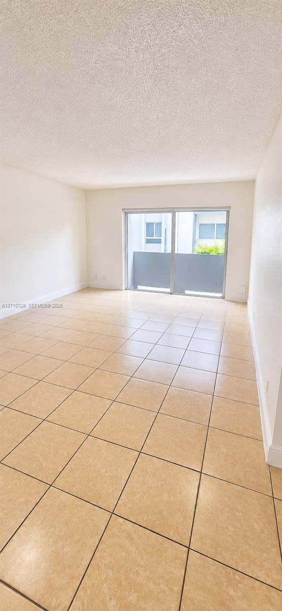 11110 SW 196th Street, #212, Cutler Bay, Cutler Bay, FL 33157 Interior living space featuring large-format square tile flooring, neutral walls, and a sliding glass door providing external access to a private balcony